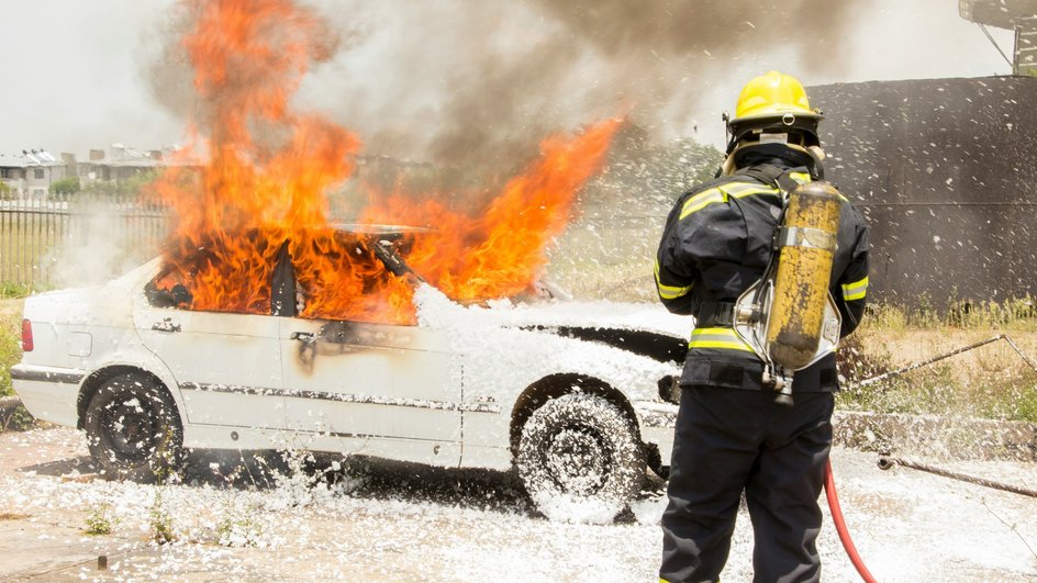 Пожарный тушит пеной белую горящую машину 