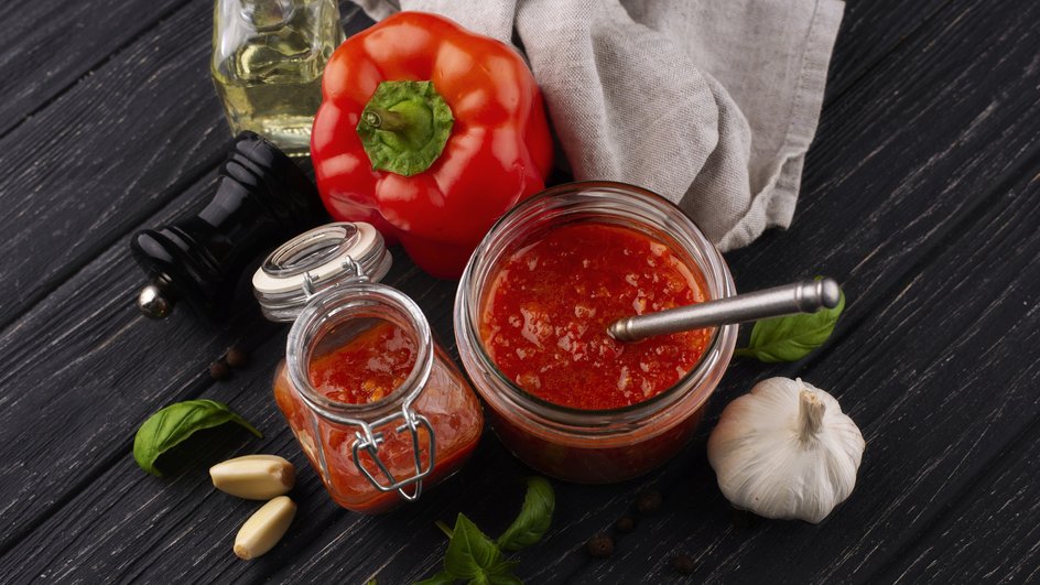 Открытые банки классического томатного соуса для мяса стоят на столе рядом с ингредиентами