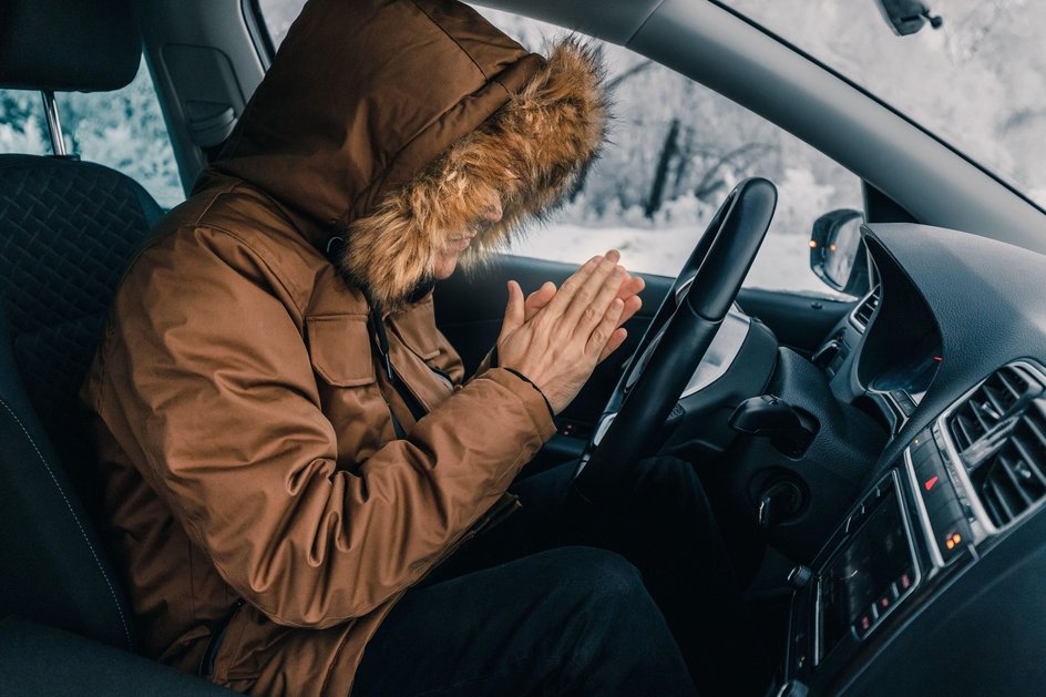 Мужчина в зимней куртке пытается согреться в салоне автомобиля