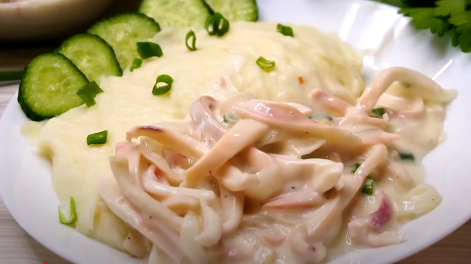Кальмары в сметанном соусе с картофельным пюре и огурцами на тарелке