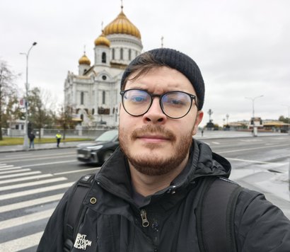 Молодой человек в черной куртке, черной шапке и очках делает селфи на фоне Храма Христа Спасителя