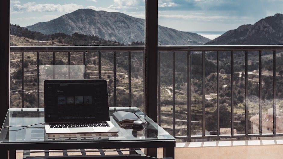 Ноутбук стоит на столе на фоне гор