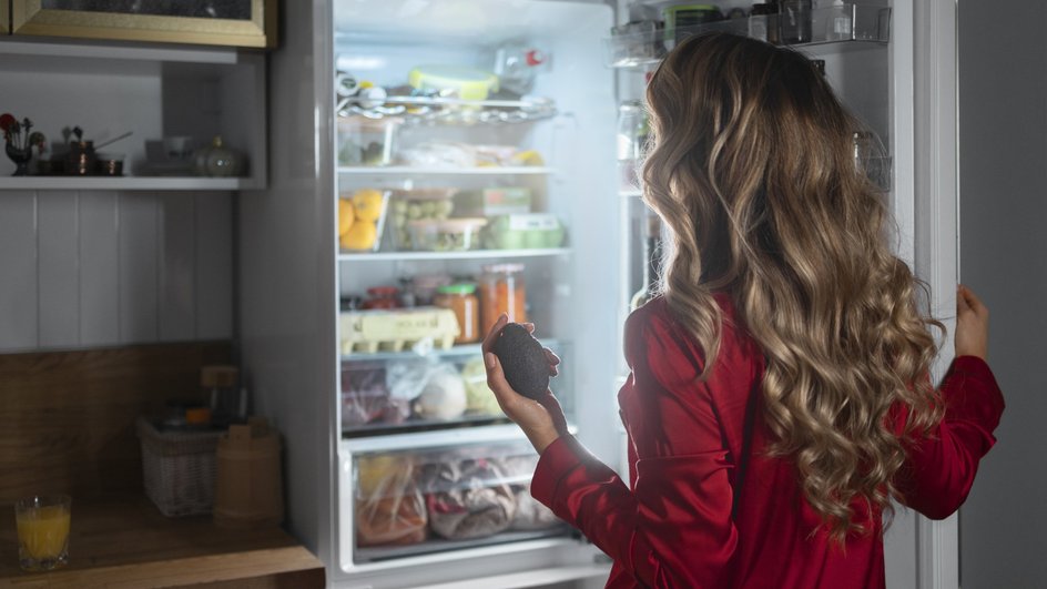 Девушка смотрит в переполненный продуктами холодильник Девушка смотрит в переполненный продуктами холодильник