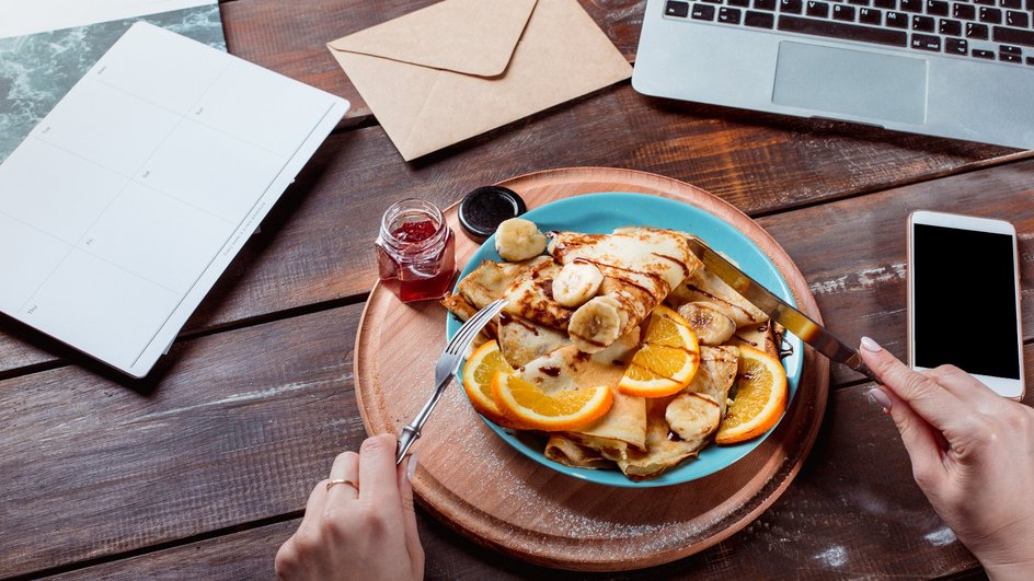 Тарелка с едой стоит на столе рядом с ноутбуком и телефоном 