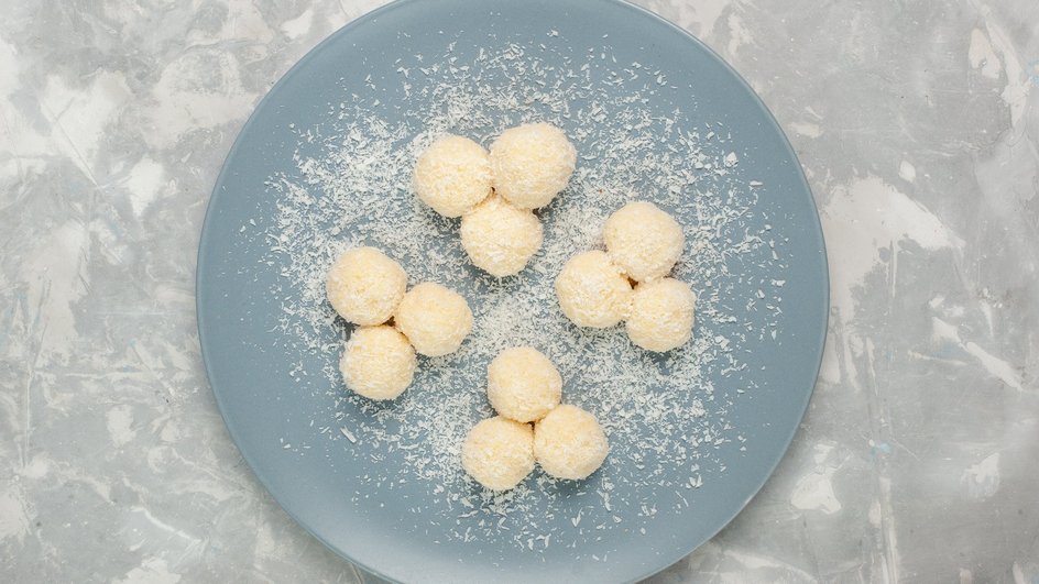 Шарики из сгущенного молока, кокосовой стружки и сливочного масла для бала баяна лежат на тарелке Шарики из сгущенного молока, кокосовой стружки и сливочного масла для бала баяна лежат на тарелке