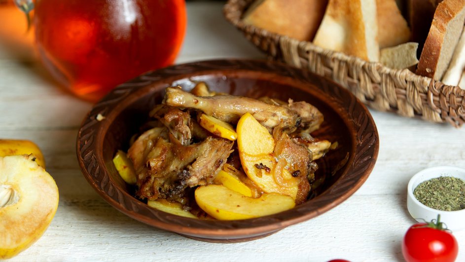 Гусь кусочками с картофелем и овощами лежит на тарелке 