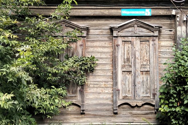 Окна со ставнями деревянного домика среди деревьев Окна со ставнями деревянного домика среди деревьев