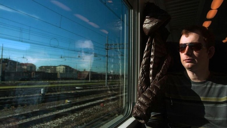 Мужчина в вагоне в темных очках путешествует по России, смотрит в окно.