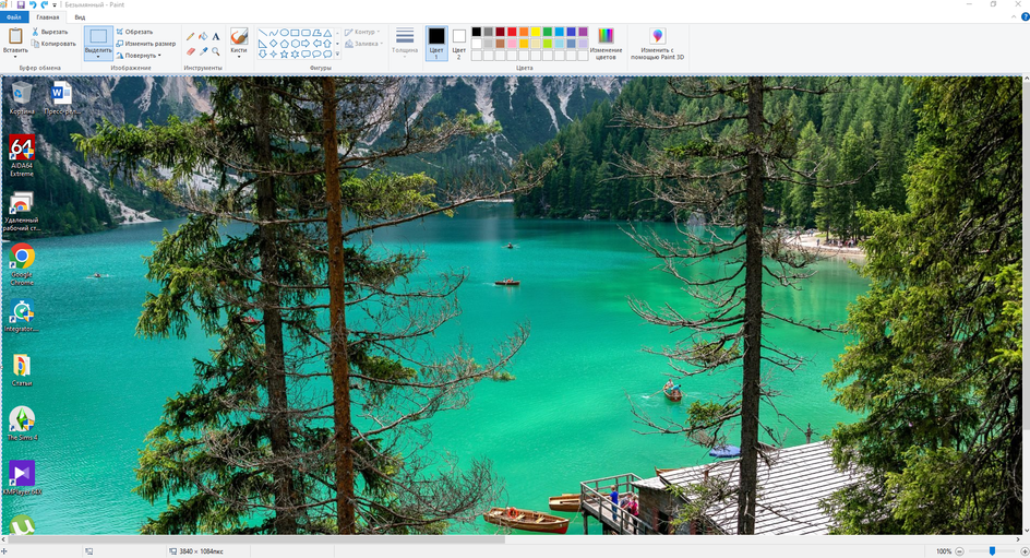 На экране компьютера открыта программа Paint с изображением живописного озера. На переднем плане видны деревья, а за ними — ярко-бирюзовая вода озера. На озере плавают несколько лодок. Вдали виднеются лесистые горы. На рабочем столе слева расположены иконки программ и папок, таких как Корзина, AIDA64 Extreme, Удаленный рабочий стол, Google Chrome, Integrator, Статьи, The Sims 4 и KMPlayer.