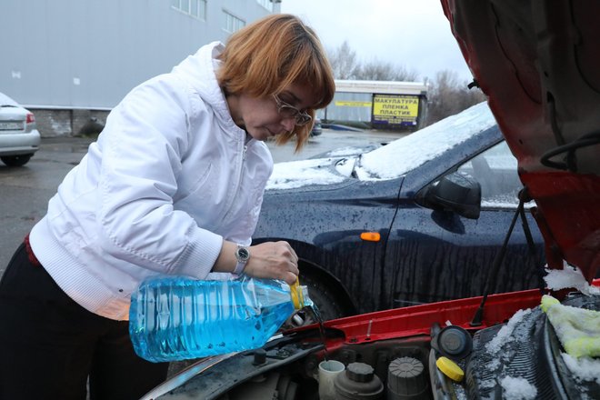 Женщина заливает незамерзайку в бачок своей машины