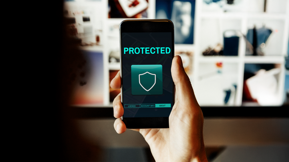 Смартфон в руке человека, на экране смартфона показан щит, символизирующий отсутствие вирусов Смартфон в руке человека, на экране смартфона показан щит, символизирующий отсутствие вирусов