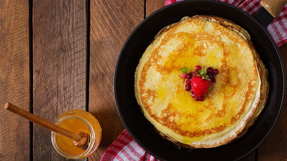 Постные блины из кукурузной муки лежат на тарелке рядом с банкой меда