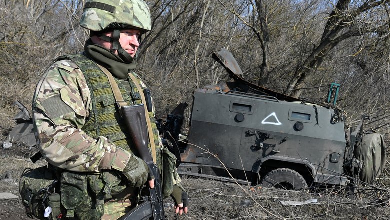 Военнослужащий РФ рядом со сгоревшим бронеавтомобилем ВСУ «Козак» на территории освобожденной деревни Новая Сорочина в Суджанском районе Курской области.