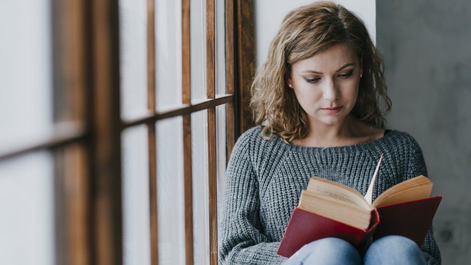 Девушка ищет в книге значение приметы, если птица залетела в окно. 