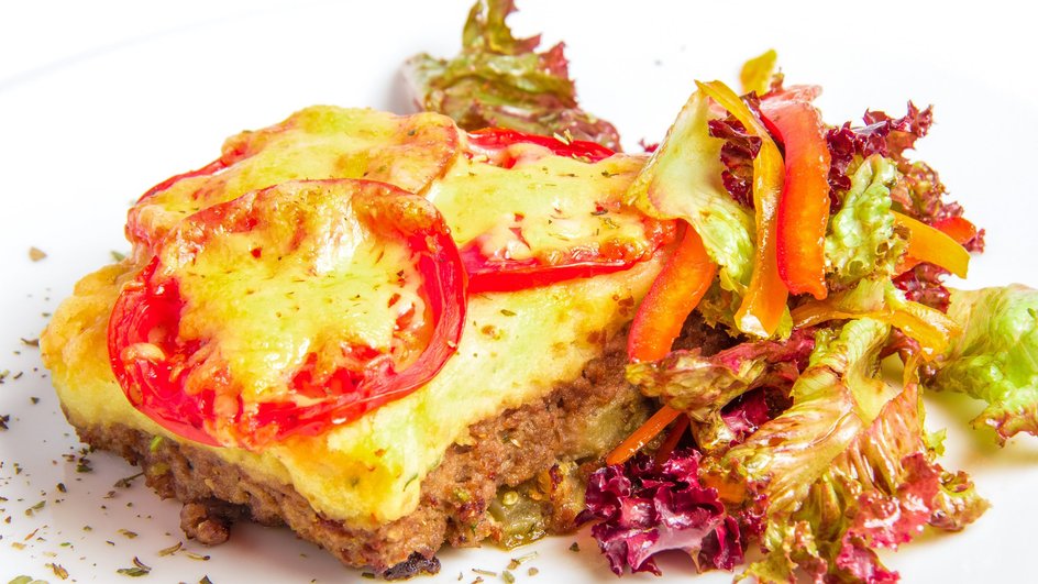 Мясо по-французски лежит на тарелке рядом с салатом