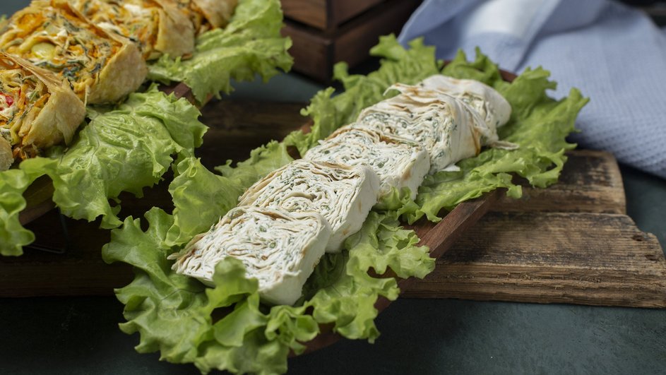 Рулеты из лаваша с сыром и огурцами лежат на листе салата