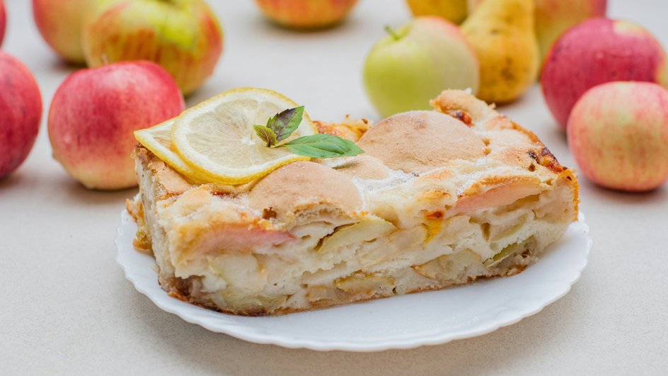 Кусочек постной шарлотки с медом лежит на тарелке рядом с яблоками